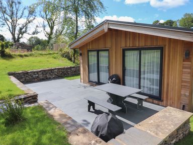 An outdoor patio area with a picnic table and benches beside a wooden building at Millstream Ridge in Haverthwaite
