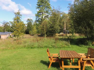 A wooden table with chairs on a grassy lawn with trees and a building in the background at Millstream Ridge in Haverthwaite