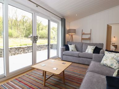 A living room with two gray sofas a wooden coffee table a striped rug a floor lamp and sliding glass doors at Hawthorn Croft in Haverthwaite