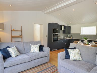 A living area with two grey sofas with cushions a kitchen with dark cabinets and a dining table at Hawthorn Croft in Haverthwaite