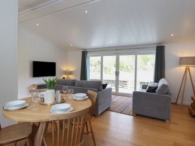A dining table with chairs and a vase of flowers next to a living room with sofas and a television at Hawthorn Croft in Haverthwaite