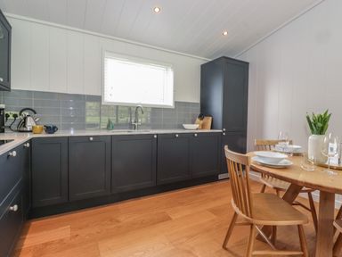 A kitchen with dark cabinets a wooden dining table with chairs and a vase with flowers at Hawthorn Croft in Haverthwaite