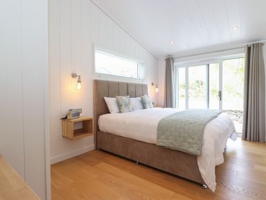 A bedroom with a large bed two bedside shelves wall lamps a window and sliding glass doors with curtains at Hawthorn Croft in Haverthwaite