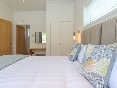 A bedroom with a bed with patterned pillows a bedside lamp a wooden door a mirror above a wooden desk and a white closet at Hawthorn Croft in Haverthwaite
