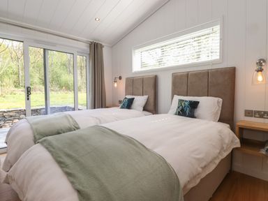 A bedroom with two single beds green blankets and pillows with a window and glass door showing outside at Hawthorn Croft in Haverthwaite