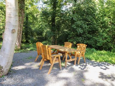 A wooden table with four chairs on a gravel area surrounded by trees and greenery at Hawthorn Croft in Haverthwaite