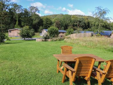 A grassy outdoor area with a wooden table and chairs and wooden cabins in the background at Hawthorn Croft in Haverthwaite