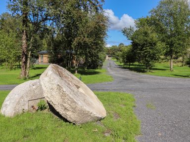 A gravel road lined with trees and two large millstones on grass at Hawthorn Croft in Haverthwaite