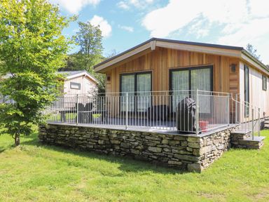 A wooden cabin with a stone foundation and metal railing on a grassy lawn at Ash Thwaite in Haverthwaite