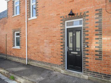 A black front door with the number 6 on a brick house with two windows at The Corner House in Weymouth
