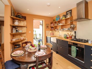 A kitchen with dark lower cabinets wooden countertop and round wooden dining table set with plates and glasses at The Corner House in Weymouth