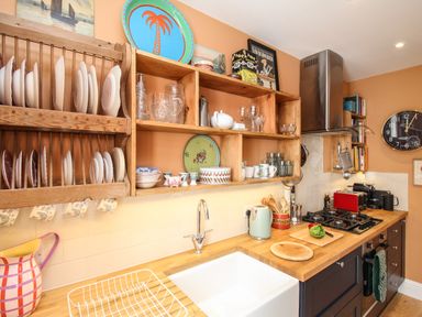 A kitchen with wooden shelves holding dishes and glasses above a sink and gas stove at The Corner House in Weymouth