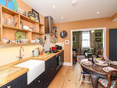 A kitchen with wooden countertops and shelves next to a dining table with plates and fruit at The Corner House in Weymouth