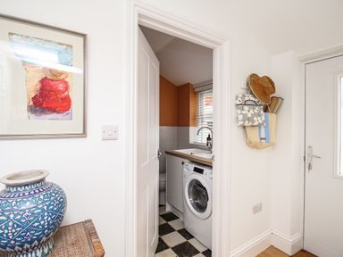 A laundry room with a washing machine a sink and window seen through an open door at The Corner House in Weymouth