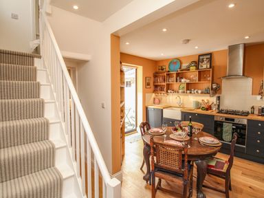 A kitchen with wooden dining table and chairs next to a staircase at The Corner House in Weymouth