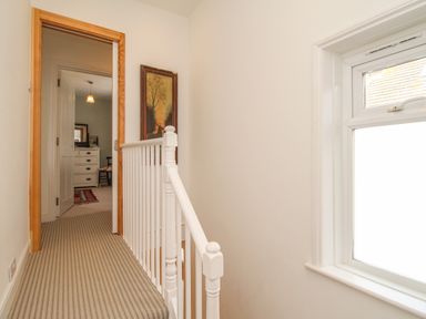 A hallway with striped carpet leading to a room with a chest of drawers and a chair at The Corner House in Weymouth