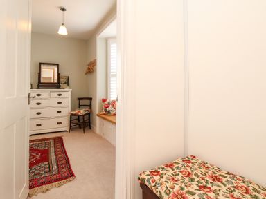 A dressing room with a white chest of drawers a chair with a floral cushion a window seat with floral cushions and a red patterned rug on the floor at The Corner House in Weymouth
