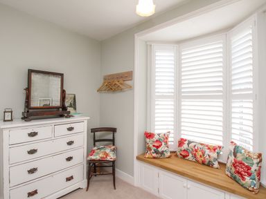 A room with a white dresser and mirror a chair with floral cushion and a window seat with floral cushions at The Corner House in Weymouth