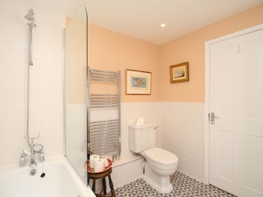 A bathroom with a bathtub shower combination a toilet a towel rack and two framed pictures on the wall at The Corner House in Weymouth