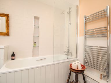 A bathroom with a bathtub shower and glass screen a towel rail and a stool with toilet paper at The Corner House in Weymouth