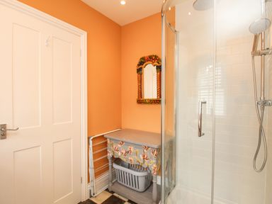 A bathroom with an orange wall a floral table a basket and a glass shower at The Corner House in Weymouth