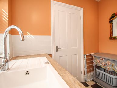 A kitchen sink with a chrome faucet next to a white door and a small table with floral patterns at The Corner House in Weymouth