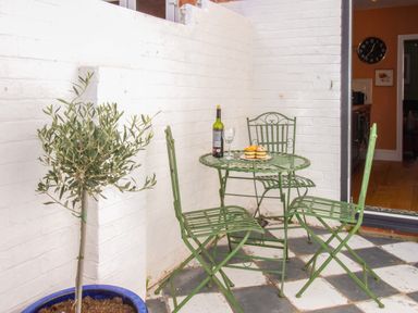 A small outdoor patio with green metal table and chairs a potted plant and a bottle of wine with cupcakes on the table at The Corner House in Weymouth