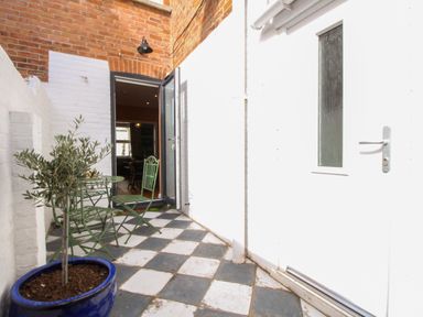 A small outdoor patio with black and white tiled floor green metal table and chairs and a potted plant at The Corner House in Weymouth