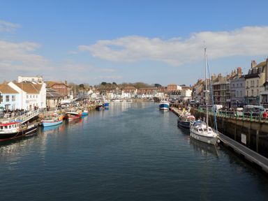 A harbor with boats docked along both sides and buildings lining the waterfront at The Corner House in Weymouth