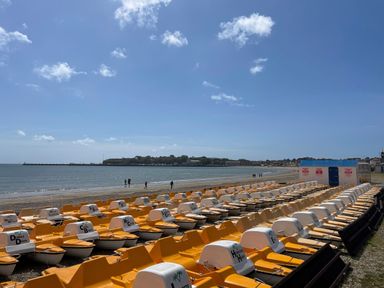 Pedal boats lined up on the beach by the sea with a few people walking along the shore at The Corner House in Weymouth