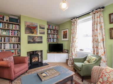 A living room with bookshelves a fireplace armchairs and a window with floral curtains at The Corner House in Weymouth