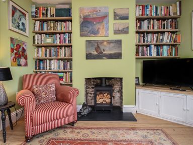 A sitting area with a striped armchair a fireplace with stacked firewood bookshelves and a television cabinet at The Corner House Weymouth