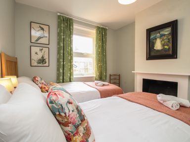 A bedroom with two beds having floral pillows and orange throws near a window with green curtains at The Corner House in Weymouth