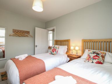 A bedroom with two wooden framed single beds with white bedding and floral cushions at The Corner House in Weymouth
