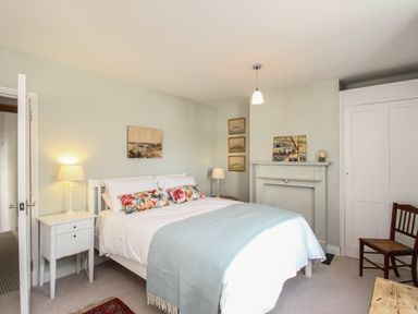 A bedroom with a double bed bedside tables lamps paintings and a chair at The Corner House in Weymouth