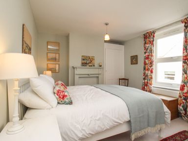 A bedroom with a bed with floral pillows and a blue throw blanket beside a window with floral curtains at The Corner House in Weymouth