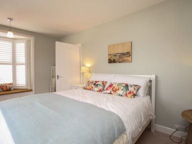 A bedroom with a bed with floral pillows and light blue throw at The Corner House in Weymouth