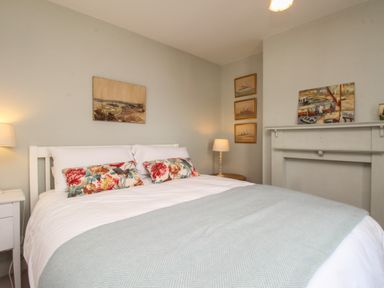 A bedroom with a double bed bedside tables lamps and paintings above the bed and mantle at The Corner House in Weymouth