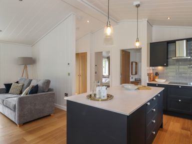 A kitchen island with stools and pendant lights next to a gray sofa and wooden floor at The Brambles in Haverthwaite