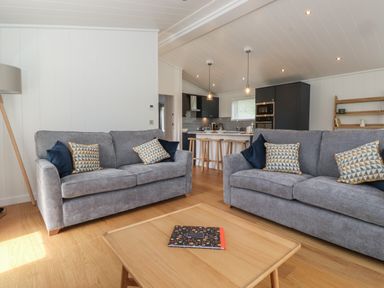 A living room with two gray sofas and patterned cushions facing a wooden coffee table with a book in a kitchen open plan at The Brambles in Haverthwaite