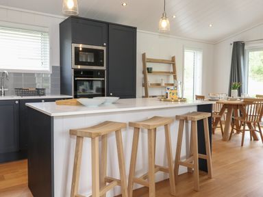 A kitchen with an island counter and wooden stools with a dining table and chairs in the background at The Brambles in Haverthwaite