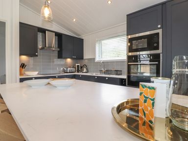 A kitchen with dark cabinets and a white countertop with plates and a tray at The Brambles in Haverthwaite