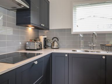 A kitchen corner with dark cabinets a stove toaster kettle coffee machine sink and window at The Brambles in Haverthwaite