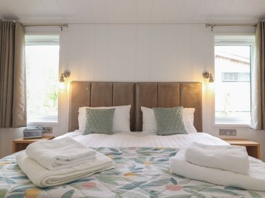 A bedroom with a bed with green pillows and folded white towels on a floral bedspread between two windows at The Brambles in Haverthwaite