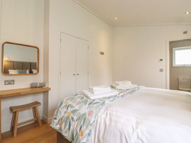 A bedroom with a bed, folded towels on the bed, a wooden stool, a wall mirror, and white paneled walls at The Brambles in Haverthwaite