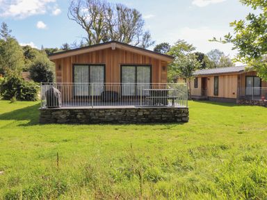 A wooden cabin with a stone base and metal railing on a porch in a grassy area at The Brambles in Haverthwaite