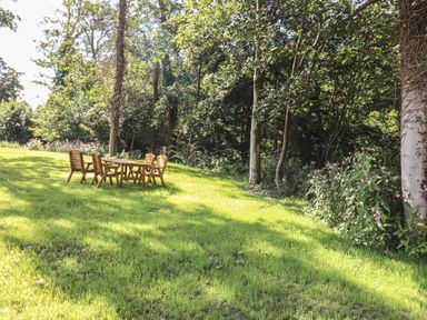 An outdoor grassy area with wooden table and chairs near trees and bushes at The Brambles in Haverthwaite