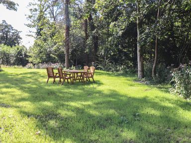 A wooden table with six wooden chairs on a grassy lawn with trees and bushes at The Burrow in Haverthwaite