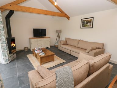A living room with sofas a wooden coffee table a fireplace and a television at The Byre in St Brides Major