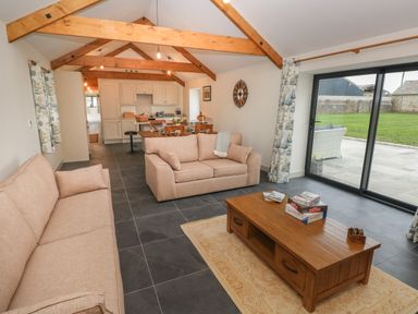 A living room with beige sofas wooden coffee table and sliding glass doors overlooking a garden at The Byre in St Brides Major